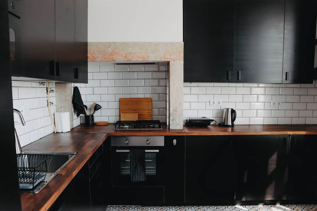 Une cuisine dotée d’un plan de travail en bois, de meubles de rangement noirs, d’une cuisinière à gaz et d’un dosseret carrelé.