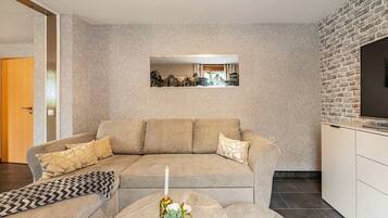 En stue med sofa, sofabord med et lys og et billede i ramme på væggen.