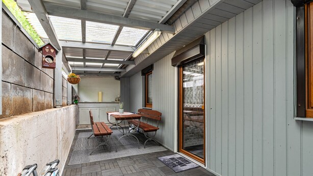 A covered patio with a table and benches, a hanging flower basket, and a door with a glass panel.