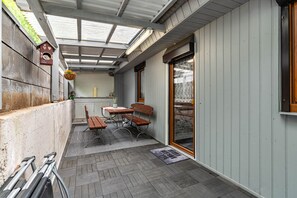 A covered patio with a table and benches, a hanging flower basket, and a door with a glass panel. - Holiday Home Mayer with Private Terrace and Wi-Fi (Idar-Oberstein)