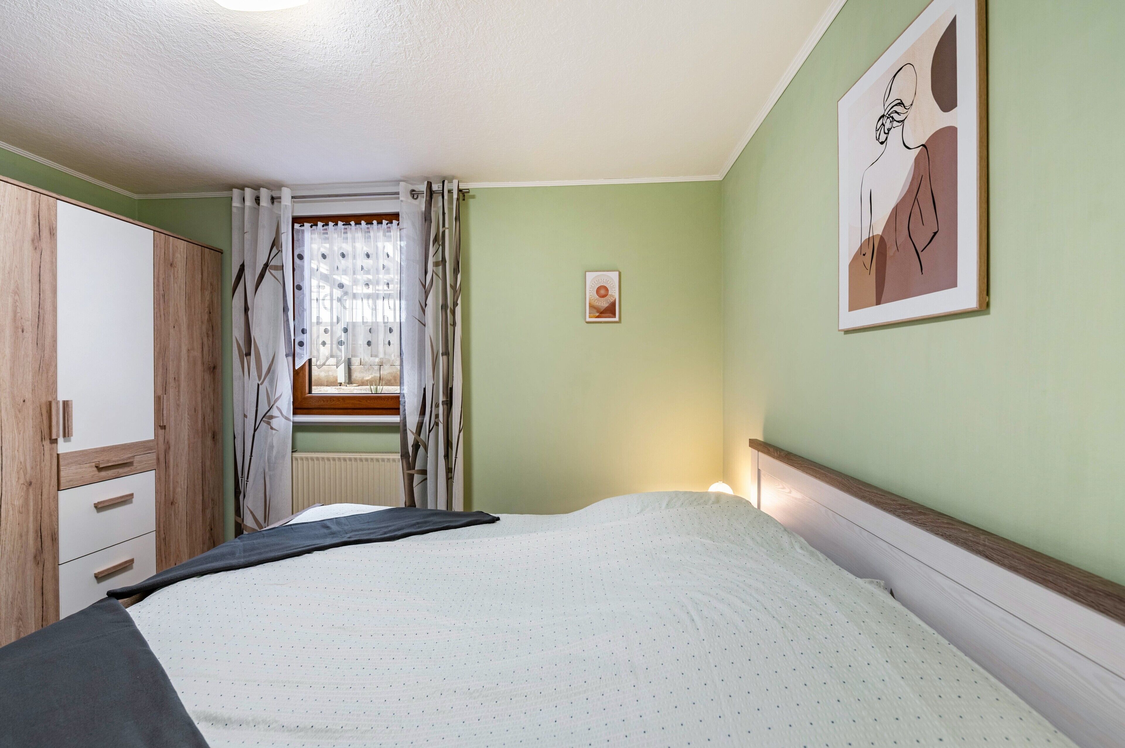 Une chambre à coucher comprenant un lit, une armoire, une fenêtre avec des rideaux et un tableau accroché au mur.