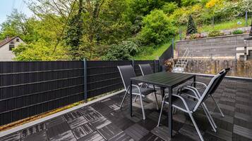 A patio with a table and chairs, a black fence, and a view of trees and a house.