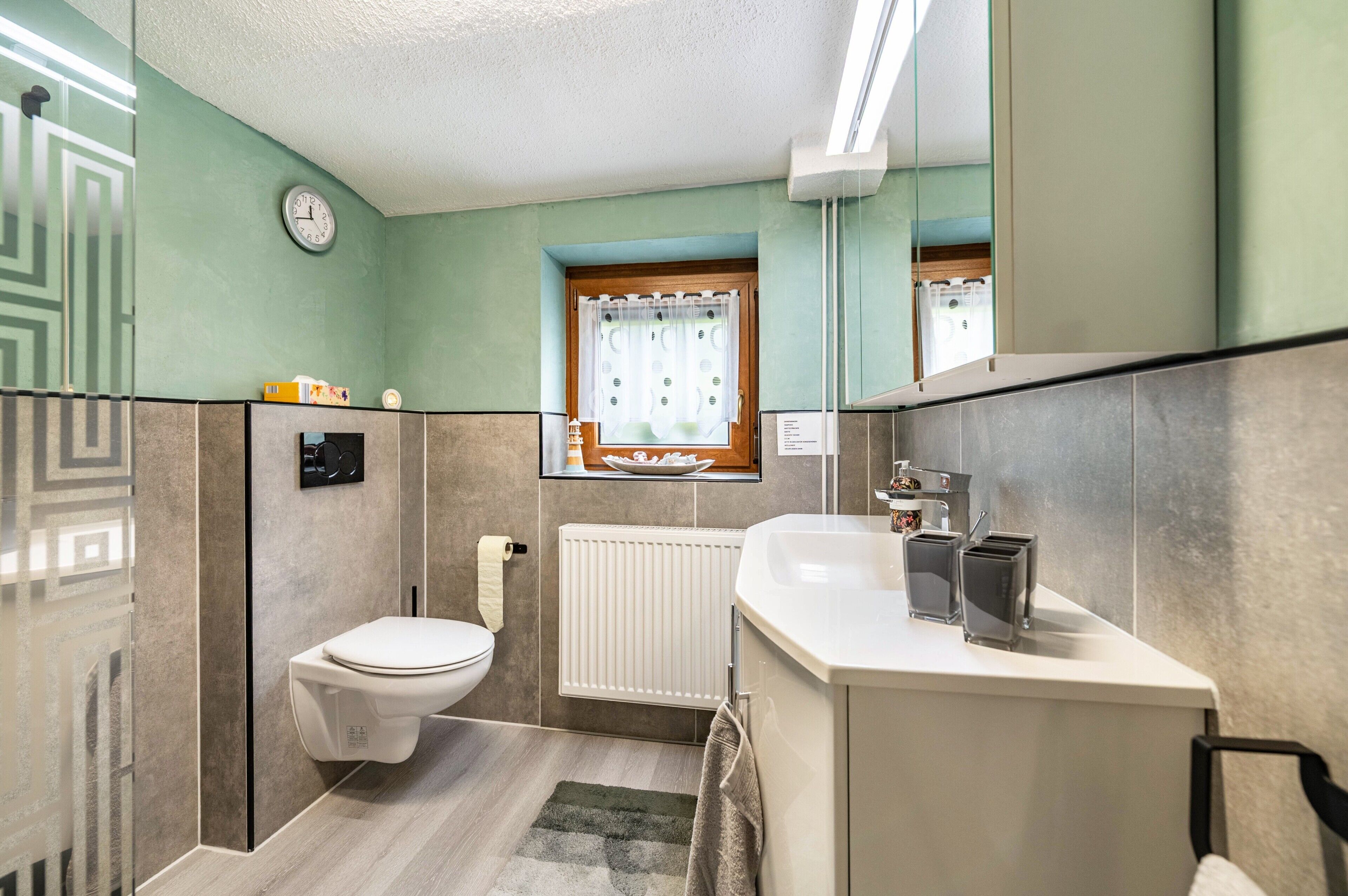 Une salle de bain équipée de toilettes, d’un lavabo, d’un miroir et d’une fenêtre avec des rideaux.