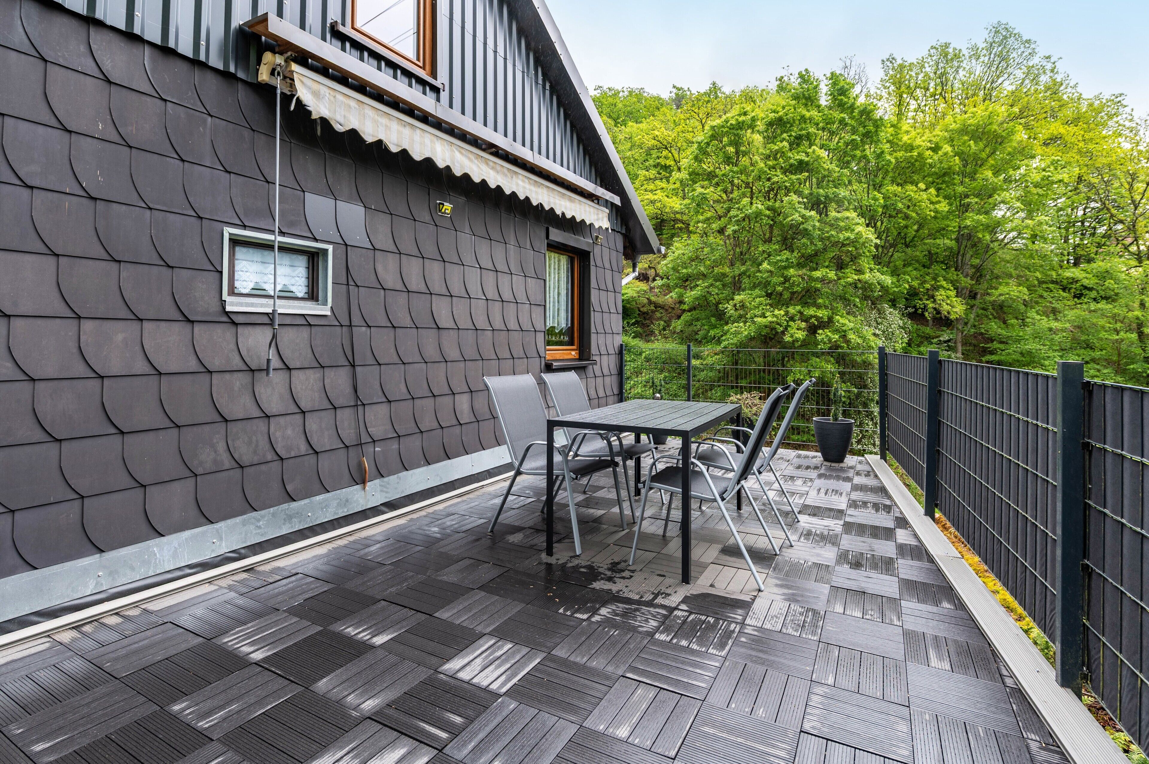 Eine Terrasse mit Tisch, Stühlen, einem Fenster und einem Metallgeländer.