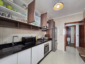 A modern kitchen with a black countertop, stainless steel appliances, wooden cabinets, and a built-in oven. - La Suite Salam , Family Oasis With Elevator (Agadir)