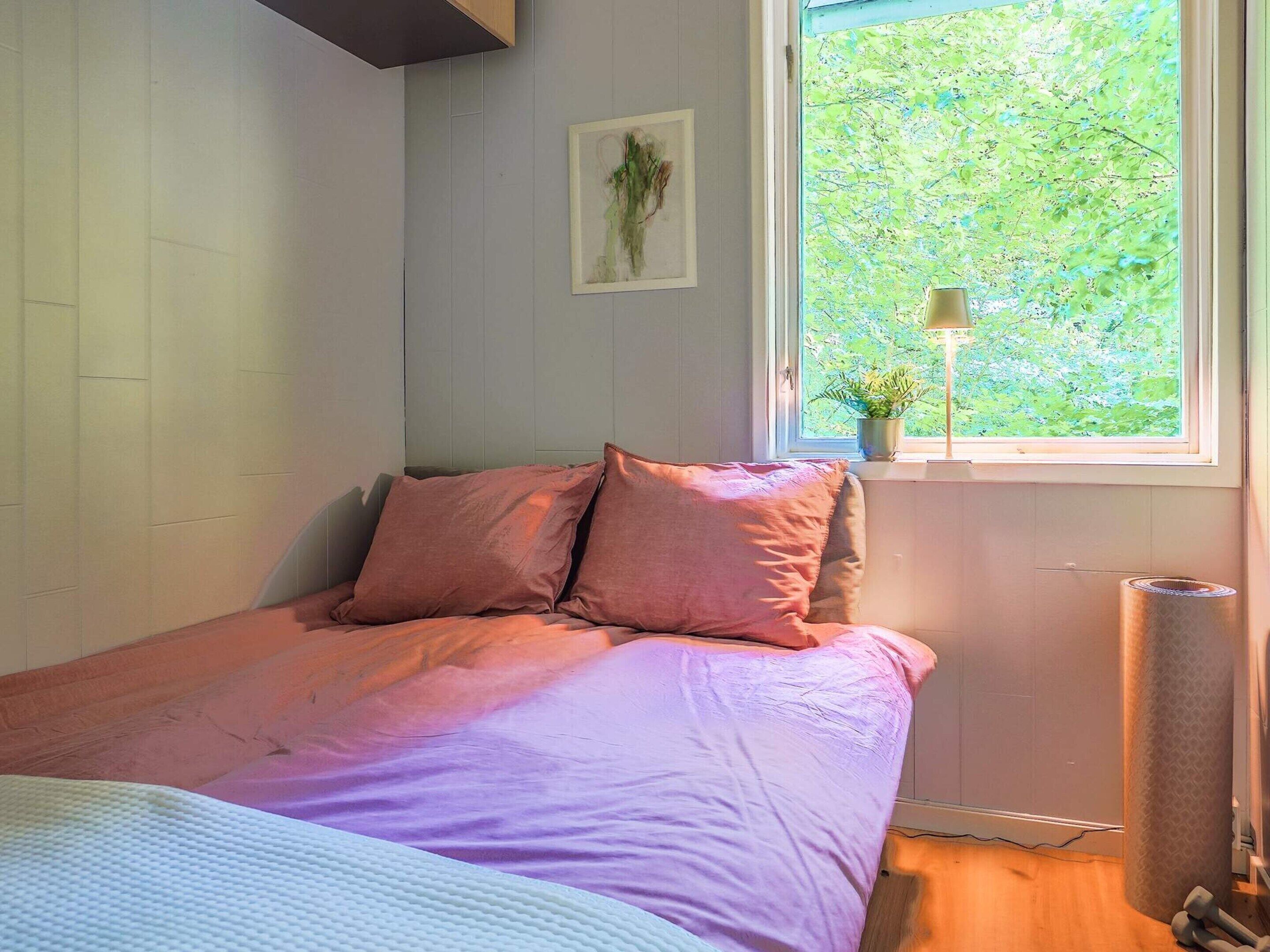 Een slaapkamer met een bed, een raam met uitzicht op groen, een radiator en een kleine plant op de vensterbank.