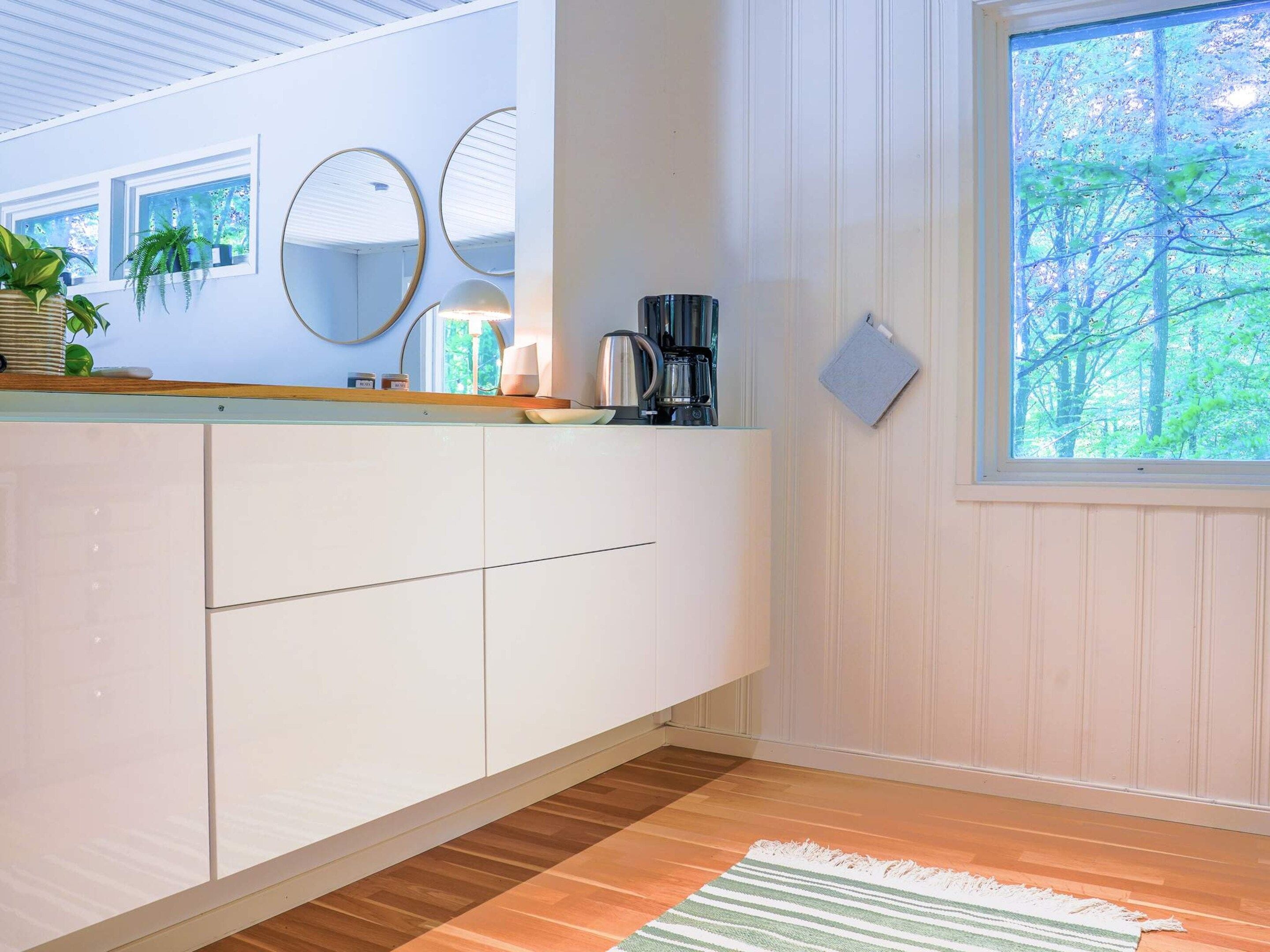 A modern kitchen with white cabinets, a coffee maker, and a window with a view of trees.