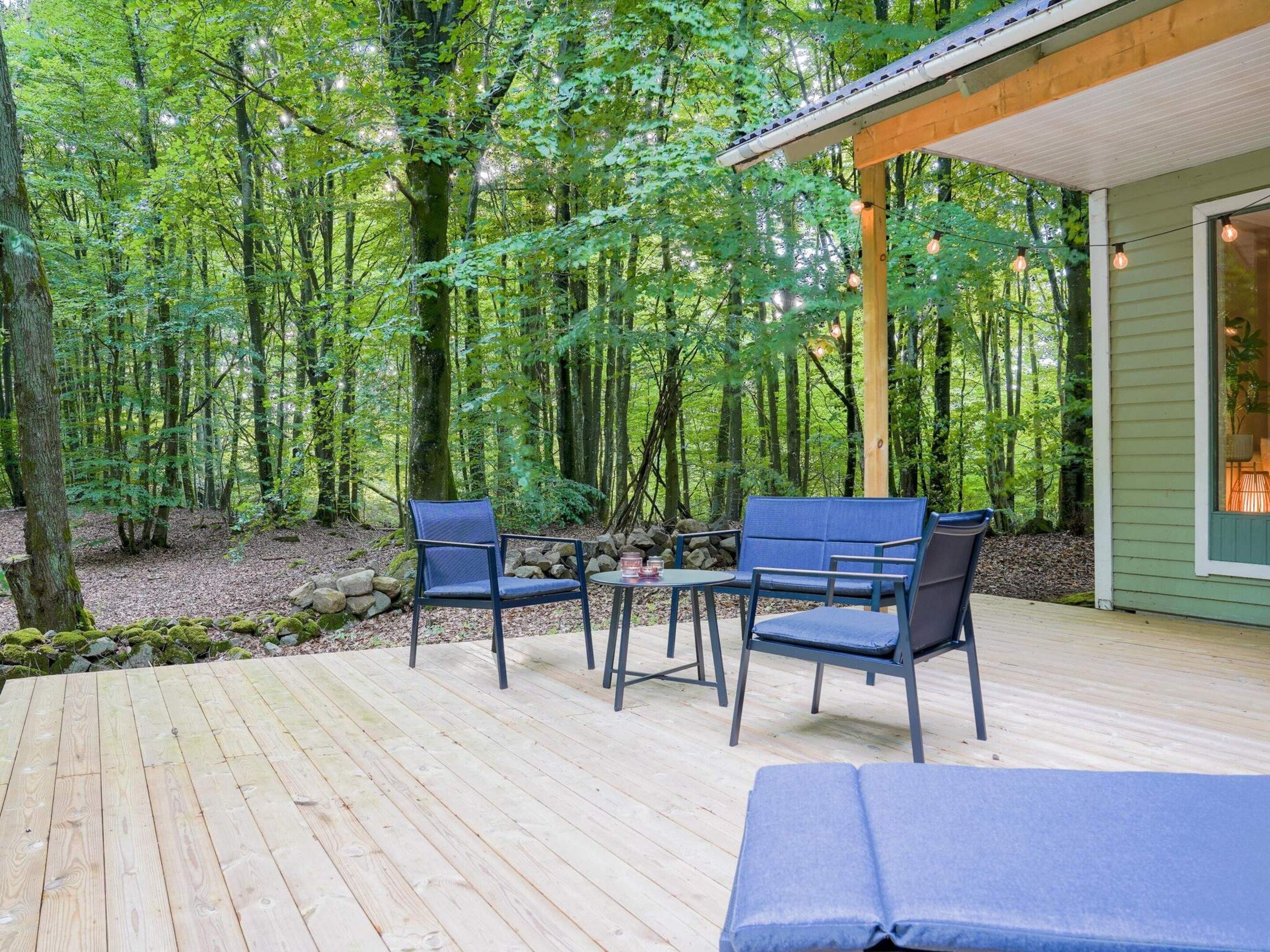 A wooden deck with outdoor furniture, surrounded by a forested area.