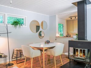 A modern interior with a round dining table, four chairs, a fireplace, and a kitchen area visible through an open door. - 4 Person Holiday Home in Horby (Horby)