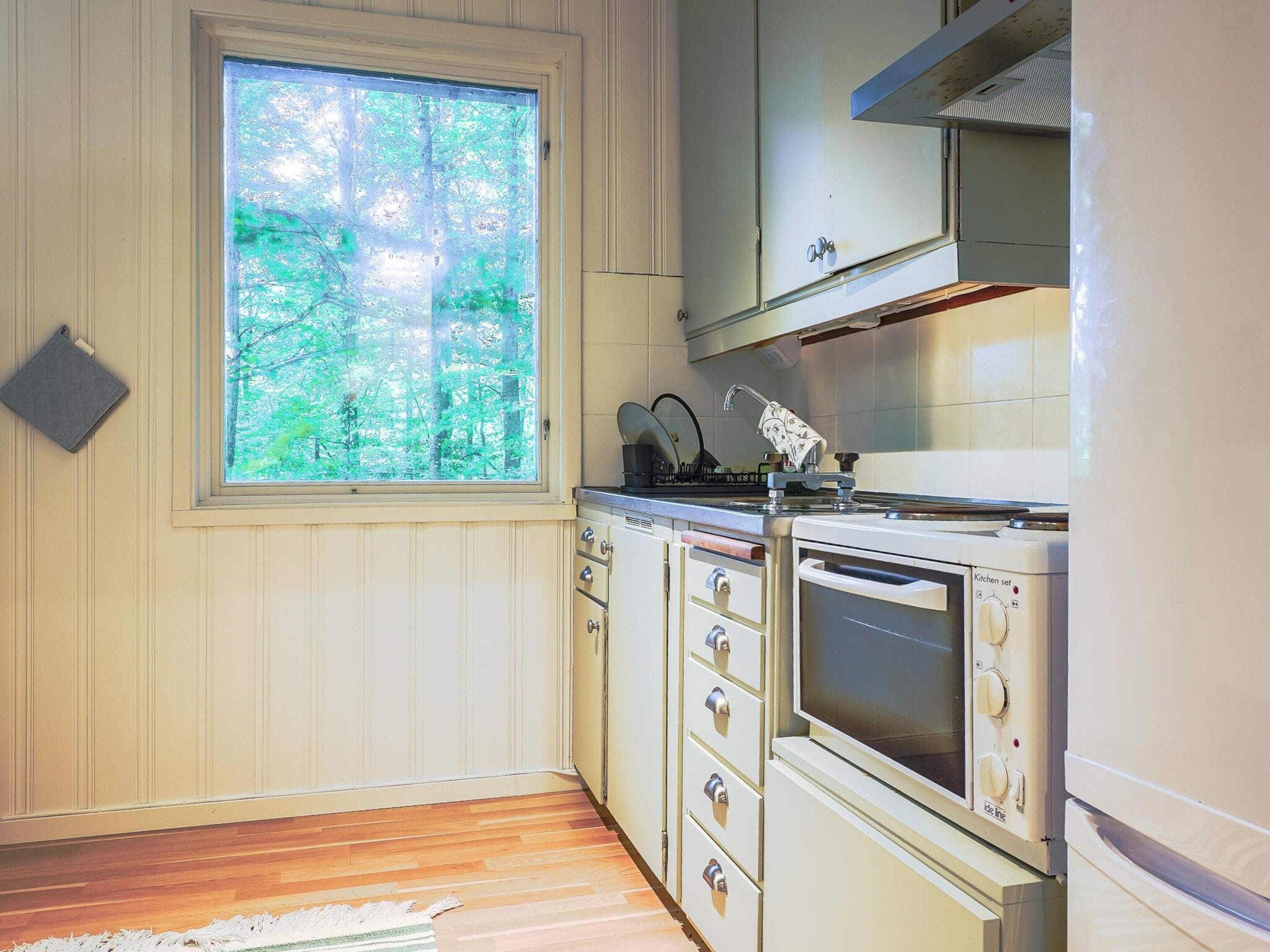 A kitchen with wooden cabinets, a stove, and a window overlooking a forest.