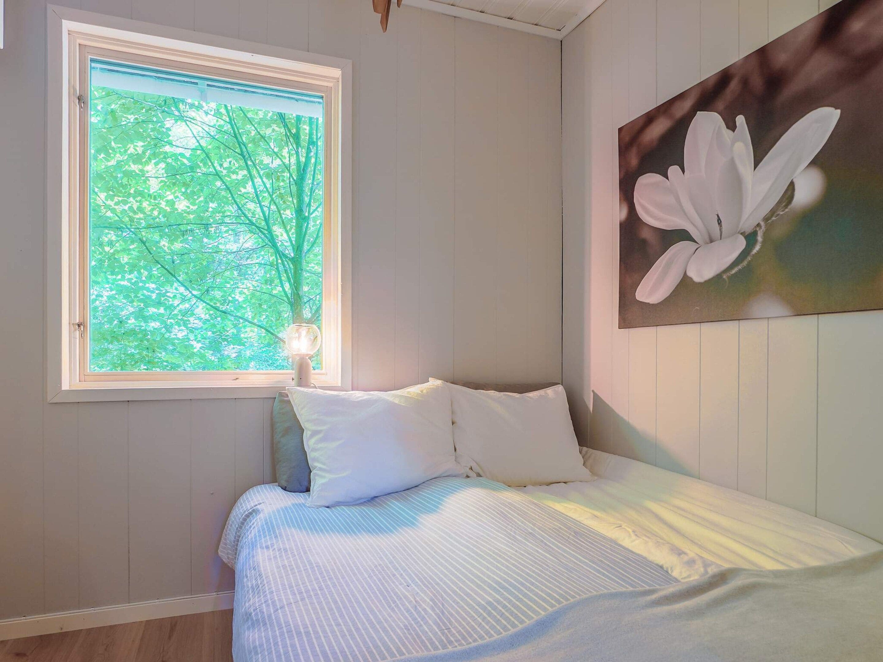 A bedroom with a bed, a window with a view of trees, and a painting of a flower on the wall.