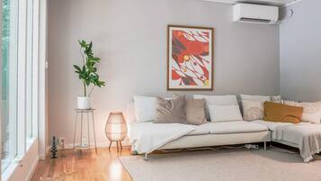 A modern living room with a sofa, a potted plant, and a framed abstract painting.