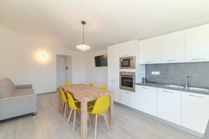 A modern kitchen with white cabinets, a microwave, oven, and a sink. There is a wooden dining table with yellow chairs. - Apartment 'Cala- Sea View Terrace' 150 Meters from Budoni Beach (Budoni)