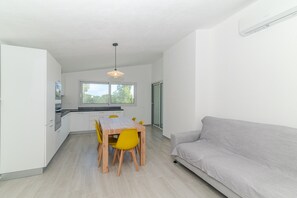 A modern kitchen with white cabinets, a wooden dining table with yellow chairs, a grey sofa, and a large window providing natural light. - Apartment 'Cala- Sea View Terrace' 150 Meters from Budoni Beach (Budoni)