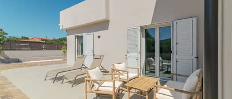 Un patio exterior con mesa y sillas, una piscina y un edificio con persianas.
