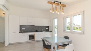 Ett modernt kök med vita skåp, ett matbord i glas och en unik lampa formgiven av rep.