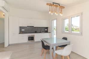 Una cocina moderna con armarios blancos, una mesa de comedor de vidrio y una lámpara de cuerda original.