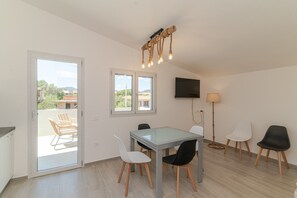 Een eetruimte met een glazen tafel, stoelen, een televisie en een lamp.