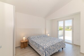 A bedroom with a bed, a nightstand, a lamp, and a sliding glass door to a balcony. - ‘Duna con Terrazza’ Apartment with Private Terrace, 3 Minutes from Budoni Beach (Budoni)