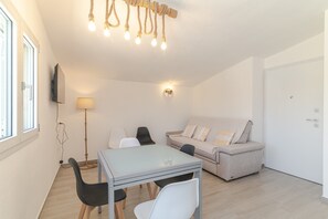 Een moderne woonkamer met een bank, een eettafel met stoelen, een lamp en een televisie aan de muur.