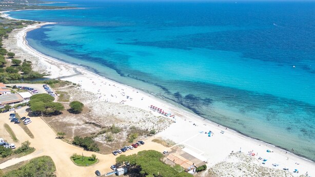 Ett flygbildsbild av ett kustområde med en strand, parkeringsplatser och byggnader.