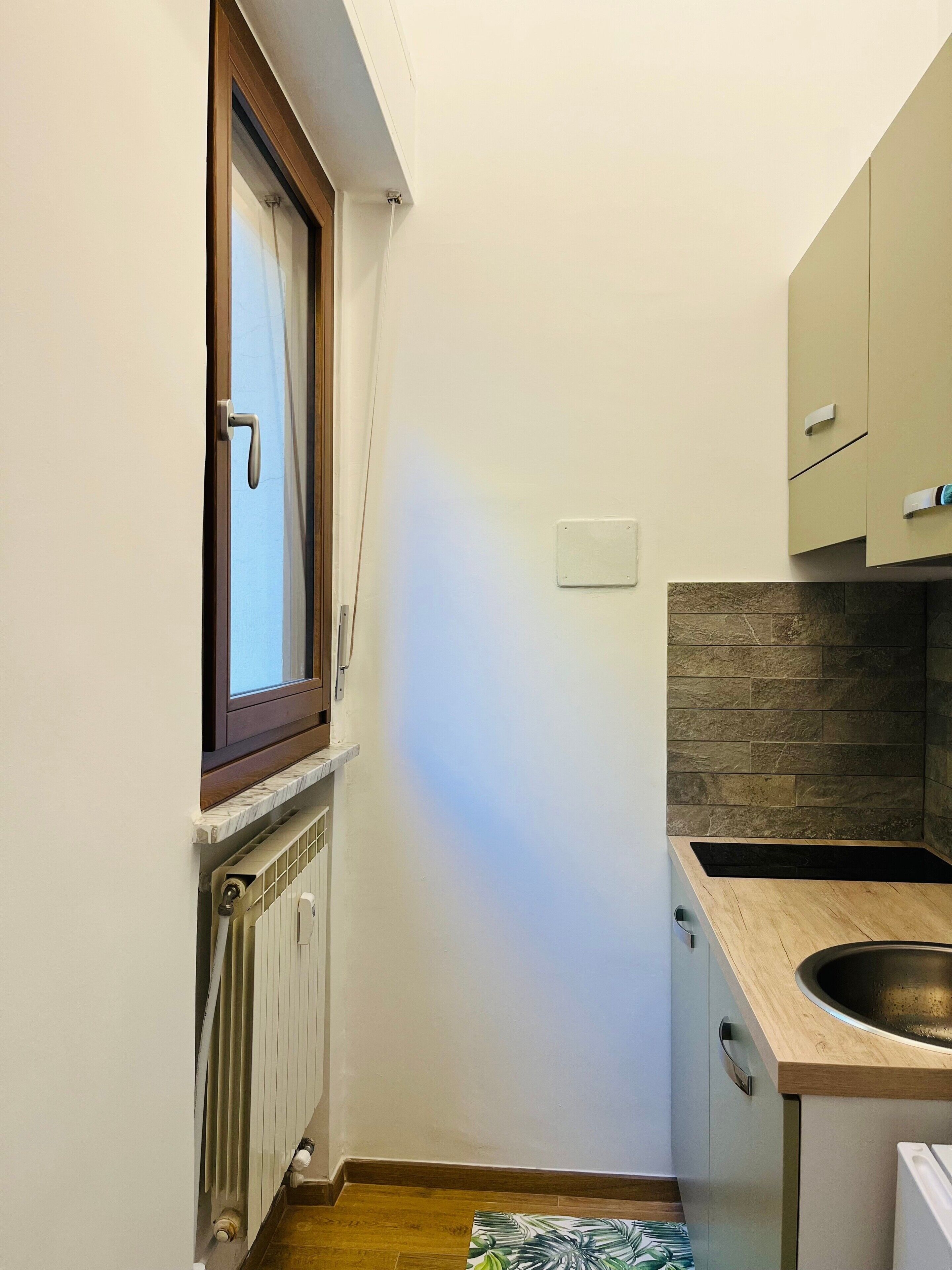 Een kleine keuken met raam, inbouwmeubels, een spoelbak en een radiator.