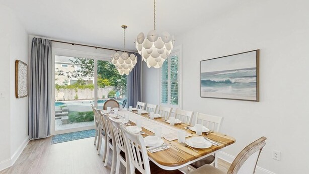 A dining area with a long table set for six, white chairs, a wooden table, and a view of the outdoors. - Gorgeous home with private pool - dog-friendly - only three blocks to the beach (Rehoboth Beach)