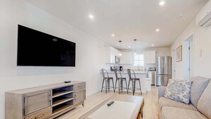 Un salón moderno con televisor de pantalla plana, una mesa de centro de madera, un sofá y una cocina al fondo.