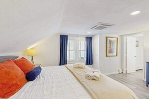 A bedroom with a bed, pillows, a bedside lamp, a window with curtains, a door, and a framed picture on the wall. - Upgraded dog-friendly home 1.5 blocks to beach with lovely backyard & pool (Rehoboth Beach)