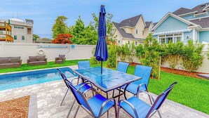Ein Garten mit Schwimmbecken, Terrassentisch und Stühlen sowie einem blauen Sonnenschirm.