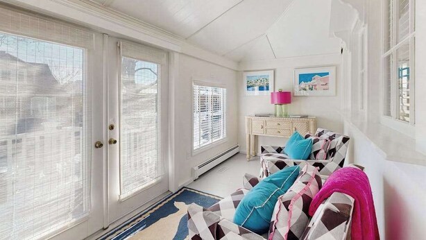 Ein Zimmer mit großem Fenster, Deckenventilator, weißer Tür, weißem Schrank und einer Couch mit gemusterten Kissen.