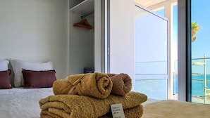 Een hotelkamer met een bed, uitzicht op zee en een stapel handdoeken.