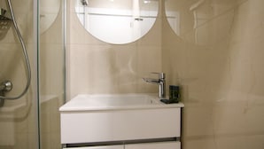 Een badkamer met een witte wastafel, een ronde spiegel en een douchehoek.