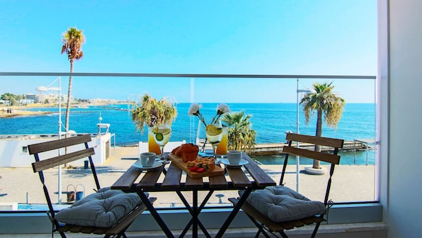 Een balkon met een tafel gedekt voor twee, met uitzicht op een strand met palmbomen en de zee.