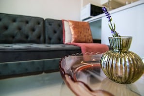 Una sala de estar con un sofá, una mesa de centro de vidrio y un jarrón con flores.