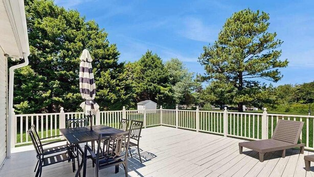 Eine Terrasse mit Tisch und Stühlen, einem Liegestuhl und einem gestreiften Sonnenschirm.
