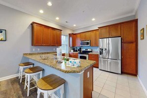 A kitchen with wooden cabinets, granite countertops, a stainless steel refrigerator, and a central island with stools. - Spacious condo w/ pool, walk to ocean and dining (Rehoboth Beach)