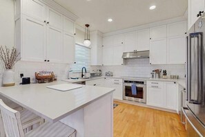 A modern kitchen with white cabinetry, a central island, stainless steel appliances, and a hanging light fixture. - Town of Rehoboth Beach spacious house w/patio, deck, grill, partial lake view (Rehoboth Beach)