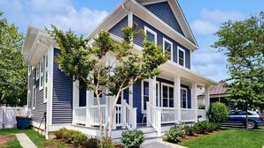 A two-story house with a porch, a tree in front, and a fence. - Home near beach with private pool, EV charger, AC, outdoor shower, yard & W/D (Rehoboth Beach)