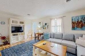Ein Wohnzimmer mit einer Couch, einem Couchtisch, einem Fernseher und einem Essbereich mit Stühlen.