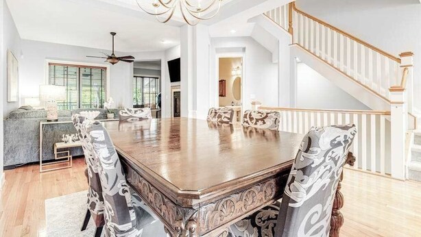 Un vaste espace dédié à la salle à manger, avec une grande table en bois, des chaises décorées, un lustre et un escalier.