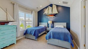 Ein Schlafzimmer mit zwei Betten, einem Schminktisch, einer Bootsdeko und einem Fenster mit Blick.