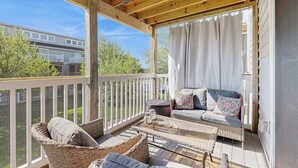 Eine überdachte Veranda mit Korbmöbeln, einem Deckenventilator und Blick auf ein Gebäude im Hintergrund.
