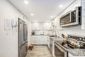 A modern kitchen with stainless steel appliances, white cabinetry, and a marble countertop. - Renovated Rehoboth Beach condo with ocean-view balcony - walk to beach (Rehoboth Beach)