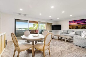 A modern living room with a round dining table, grey sofa, and a large TV. - Renovated Rehoboth Beach condo with ocean-view balcony - walk to beach (Rehoboth Beach)