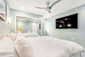 A bedroom with a bed, a ceiling fan, a TV mounted on the wall, and a mirror. - Renovated Rehoboth Beach condo with ocean-view balcony - walk to beach (Rehoboth Beach)
