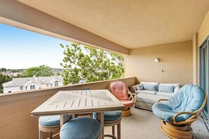 A balcony with a table and chairs, a sofa, and a wicker chair. - Renovated Rehoboth Beach condo with ocean-view balcony - walk to beach (Rehoboth Beach)