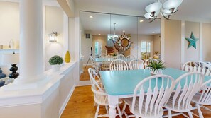 A dining area with a large table and white chairs, a chandelier, and a star decoration on the wall. - Dog-friendly townhome w/gas grill, balcony, on-site pool, tennis & basket courts (Rehoboth Beach)