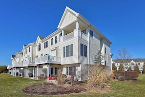 A multi-story residential building with a balcony on the second floor, a covered porch area, and a well-maintained lawn. - Dog-friendly townhome w/gas grill, balcony, on-site pool, tennis & basket courts (Rehoboth Beach)