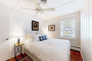 A bedroom with a bed, a ceiling fan, a window with blinds, and a nightstand with a lamp. - Town of Rehoboth Beach dog-friendly home with fireplace & W/D - walk everywhere (Rehoboth Beach)